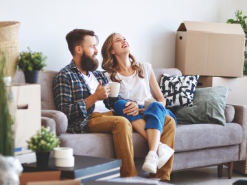 Ein Paar sitzt auf der Couch, um sie herum stehen viele Umzugskartons