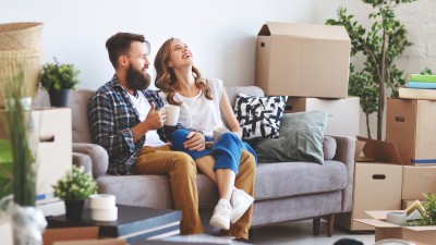 Ein Paar sitzt auf der Couch, um sie herum stehen viele Umzugskartons