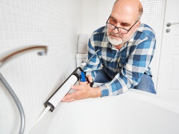 Ein Mann fugt  mit einer Kartuschenpistole eine Silikonfuge im Bad aus 