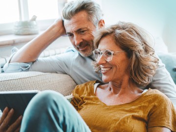 Private Rentenversicherung: Ein  Paar auf dem Sofa schaut zusammen auf ein Tablet