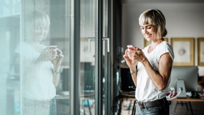 Zusatzrentenversicherung: Frau mit Handy steht vor großer Fensterfront