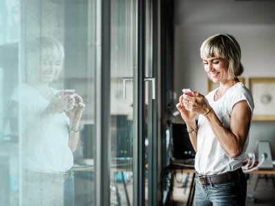 Zusatzrentenversicherung - IndexClever : Frau mit Handy steht vor großer Fensterfront