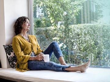 ParkKonto: Frau sitzt am Fenster und schaut in den Garten.
