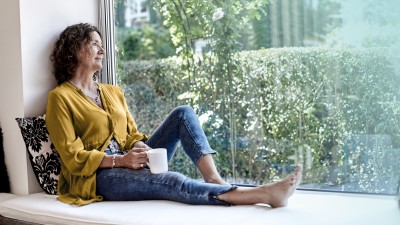 ParkKonto: Frau sitzt am Fenster und schaut in den Garten.