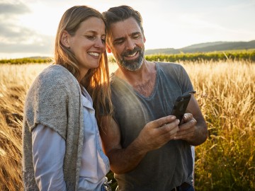 ParkKonto: Paar - im Hintergrund ein Weizenfeld - schauen entspannt auf das Smartphone
