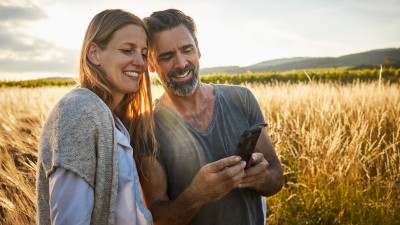 ParkKonto: Paar - im Hintergrund ein Weizenfeld - schauen entspannt auf das Smartphone