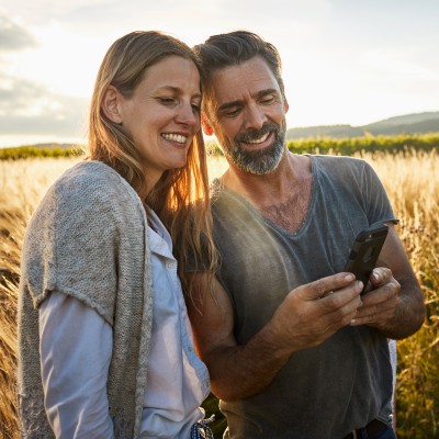 ParkKonto: Paar - im Hintergrund ein Weizenfeld - schauen entspannt auf das Smartphone