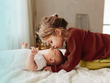 Kleines Mädchen kniet über ein Baby und küsst die Stirn des Babys