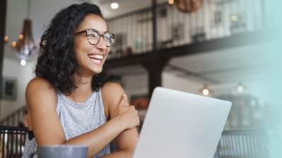 Junge Frau sitzt lächelnd vor einem Laptop