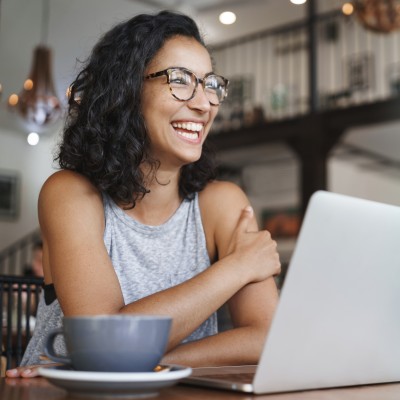 Junge Frau sitzt lächelnd vor einem Laptop
