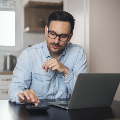 Steuern & private Rentenversicherung: Mann sitzt vor einem Laptop und berechnet etwas auf einem Taschenrechner