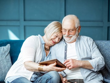 Ein Rentnerpaar auf einer blauen Couch mit einem Tablet