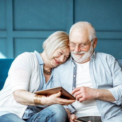 Ein Rentnerpaar auf einer blauen Couch mit einem Tablet