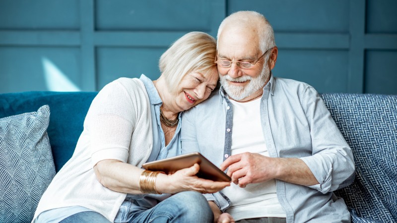 Ein Rentnerpaar auf einer blauen Couch mit einem Tablet