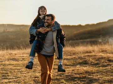 Mann tr&auml;gt Frau Huckepack auf einem Feldweg