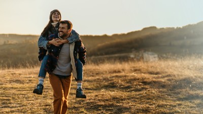 Mann tr&auml;gt Frau Huckepack auf einem Feldweg