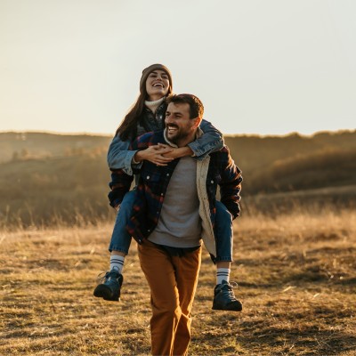 Mann tr&auml;gt Frau Huckepack auf einem Feldweg