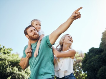Ein Mädchen hängt am Rücken ihres Vaters, die Mutter steht daneben und stützt es