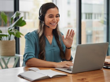 Eine Frau mit Headset vor einem Laptop bei einer Videokonferenz