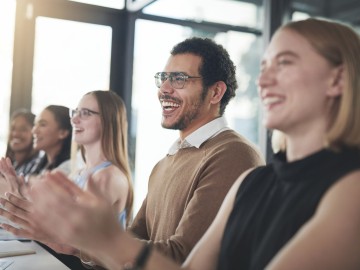 Eine Gruppe von Business-Leuten sitzen nebeneinander am Tisch und klatschen