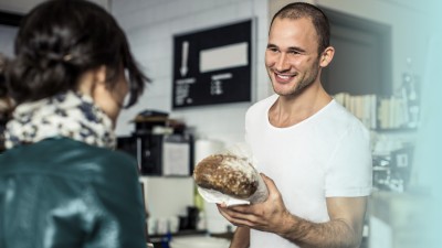 Bäckerei & Konditorei: Bäcker reicht Kundin ein Brot