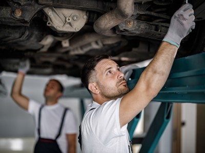 Kfz-Werkstatt: Mechaniker arbeiten an einem Unterboden