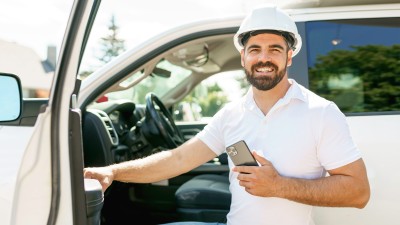 Flottenversicherung: Mann mit Smartphone steigt in ein Auto