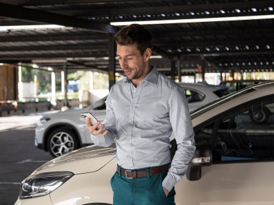 Gewerbliche Kfz-Versicherung: Geschäftsmann steht vor einem Auto und schaut auf sein Smartphone