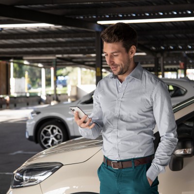 Gewerbliche Kfz-Versicherung: Geschäftsmann steht vor einem Auto und schaut auf sein Smartphone