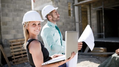 Bauleistungsversicherung: Mann und Frau stehen mit Schutzhelm auf Baustelle