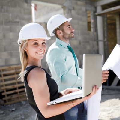Bauleistungsversicherung: Mann und Frau stehen mit Schutzhelm auf Baustelle