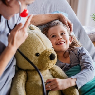 Krankenzusatzversicherung für Ihr Kind: Kleines Mädchen liegt im Bett mit einem Teddybär