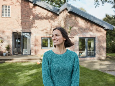 Private Pflegezusatzversicherung: Eine Frau mittleren Alters steht lächelnd vor einem Haus