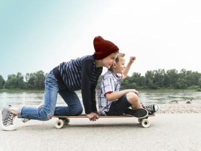 Kinderunfallversicherung: Zwei Jungs auf dem Skateboard am Flußufer