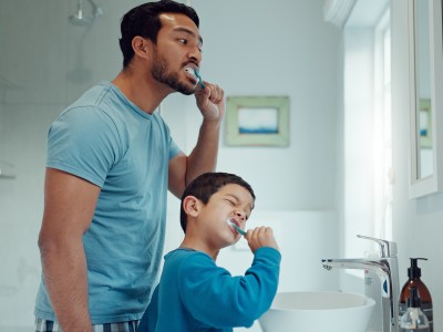 Zahnzusatzversicherung bei laufender Behandlung: Vater und Sohn putzen sich vor dem Spiegel die Zähne