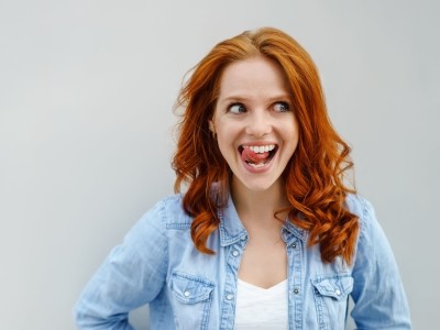 Ist eine Zahnzusatzversicherung sinnvoll oder nicht?  : Rothaarige Frau streicht mit Ihrer Zunge über Ihre gepflegten Zähne