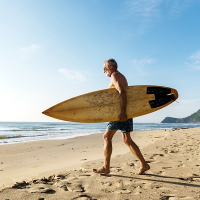 Unfallversicherung von der Steuer absetzen: Senior mit dem Surfbrett am Strand