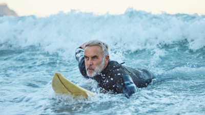 Unfallversicherung im Ausland  : Senior auf einem Surfboard in den Wellen