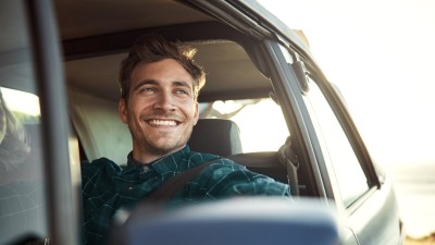 Fahrerschutzversicherung: Junger Mann schaut glücklich aus sein Auto