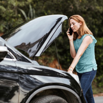 Mobilitätsschutz-Versicherung: Frau mit Autopanne ruft mit Smartphone Hilfe