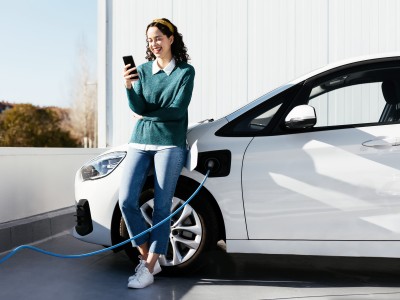 Elektroauto- & Hybrid-Versicherung: Junge Frau mit Ihrem Fahrzeug an der E-Ladestation