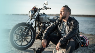 Motorradversicherung: Mann sitz vor seinem Motorrad am Wasser