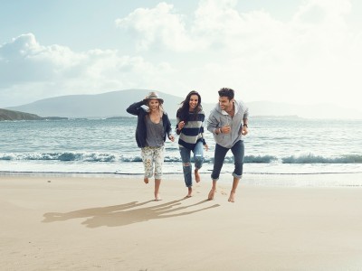Hausratversicherung für Studenten: Drei junge Menschen sprinten an einem Strand