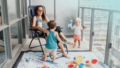 Haus- & Grundbesitzerhaftpflicht: Junge Mutter spielt mit zwei Kindern auf dem Balkon