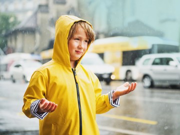Kind im Regenmantel steht in starkem Regen auf Straße