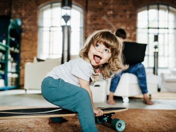 Wohnen: Kleines Kind sitzt auf einem Skateboard und streckt die Zunge raus