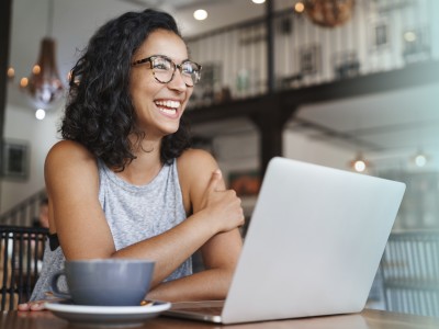 Junge Frau sitzt lächelnd vor einem Laptop